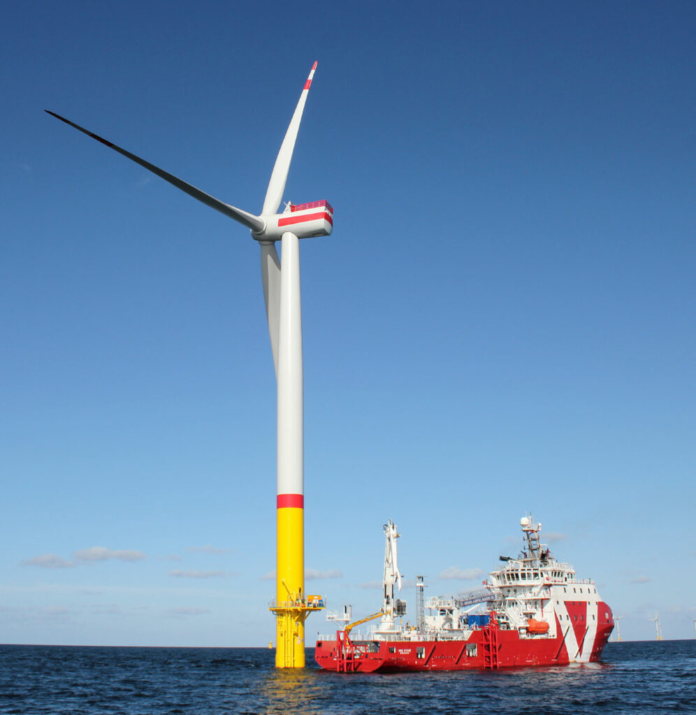 Red vessel infront of a wind turbine.