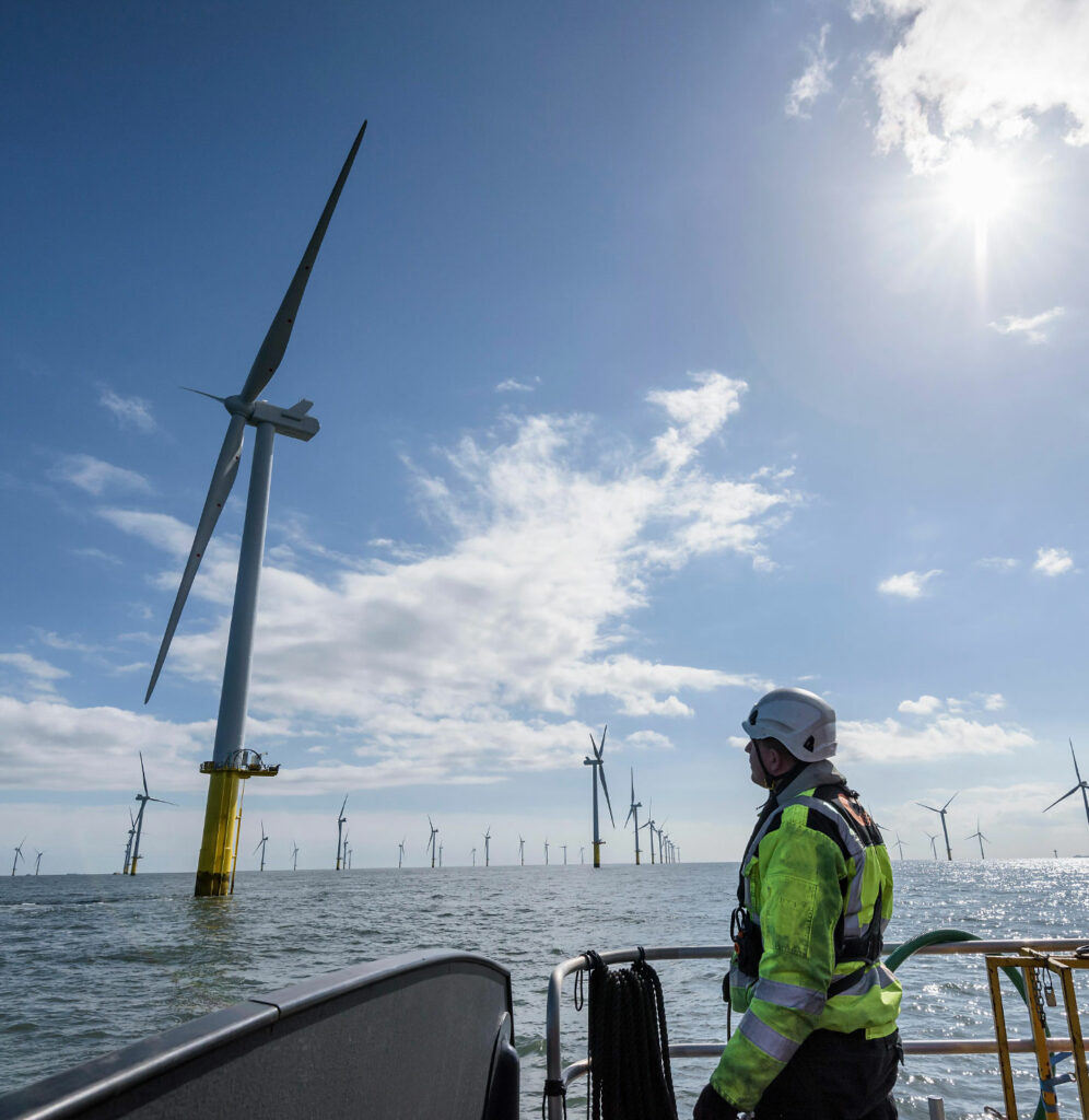 Man in yellow safety gear looking at a wind turbine.